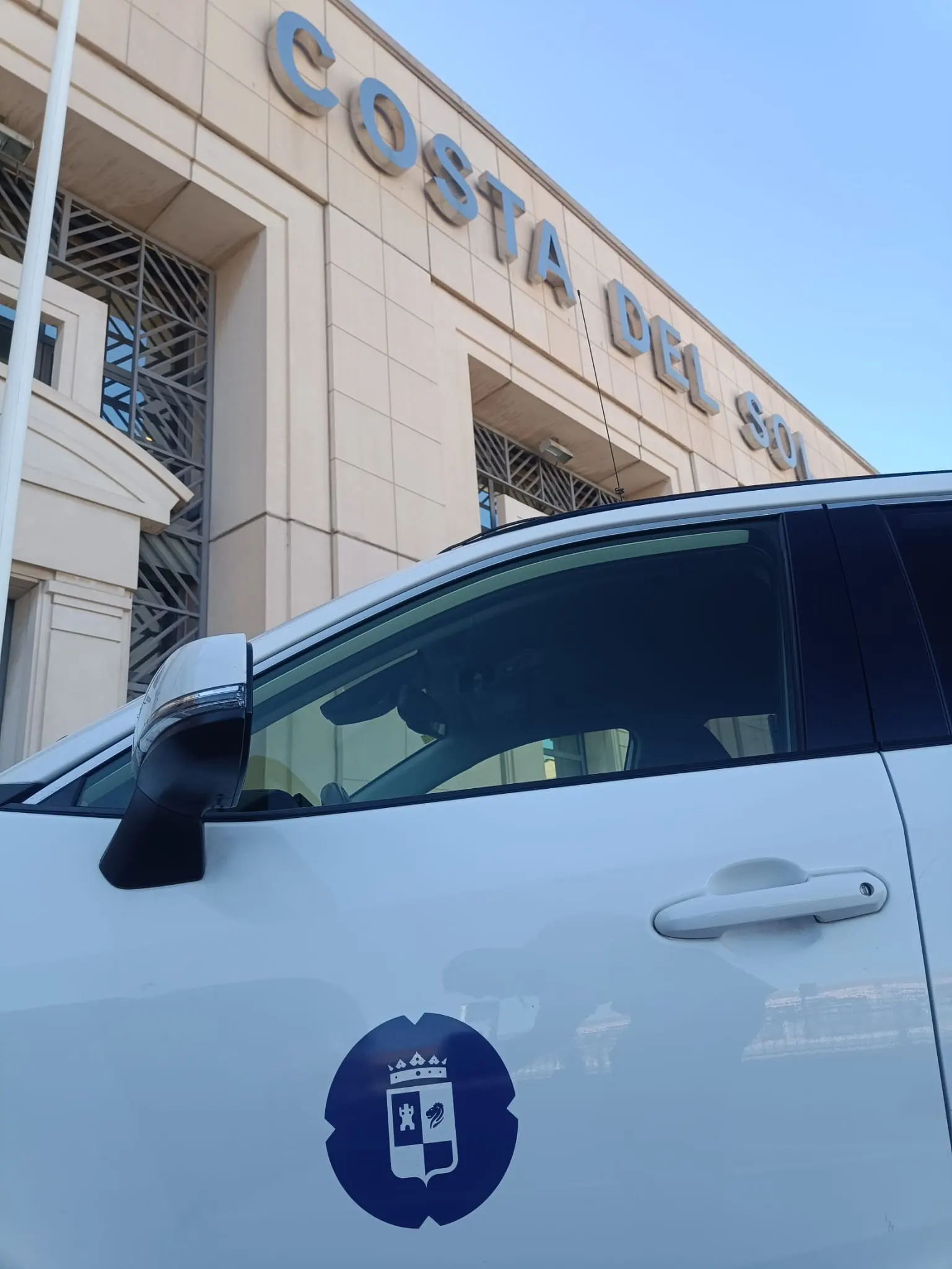 Puerta del taxi de Torrox con el escudo municipal ante el rótulo Costa del Sol de la terminal del Aeropuerto de Málaga