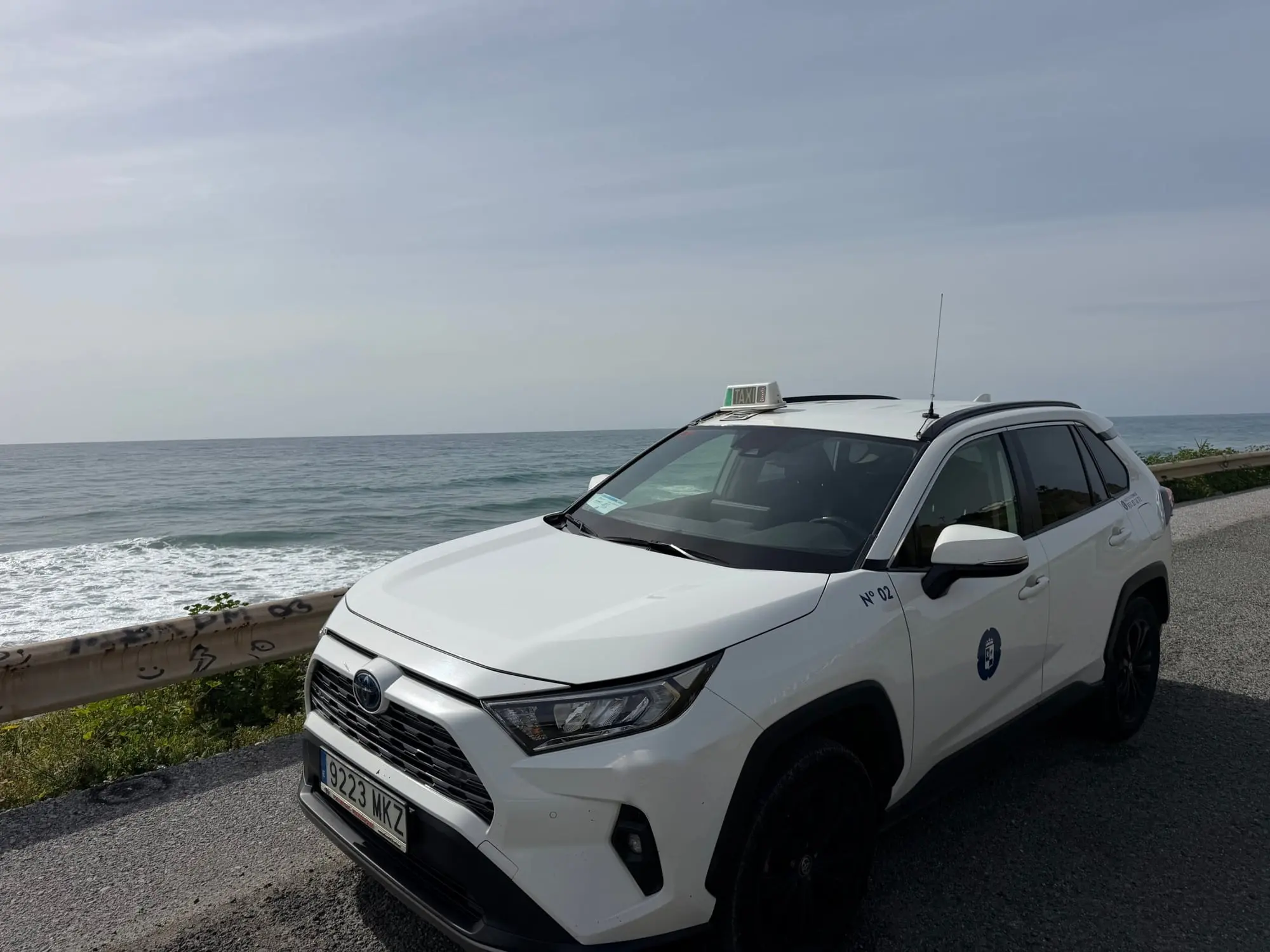 Taxi de Torrox aparcado en una carretera junto al mar con olas